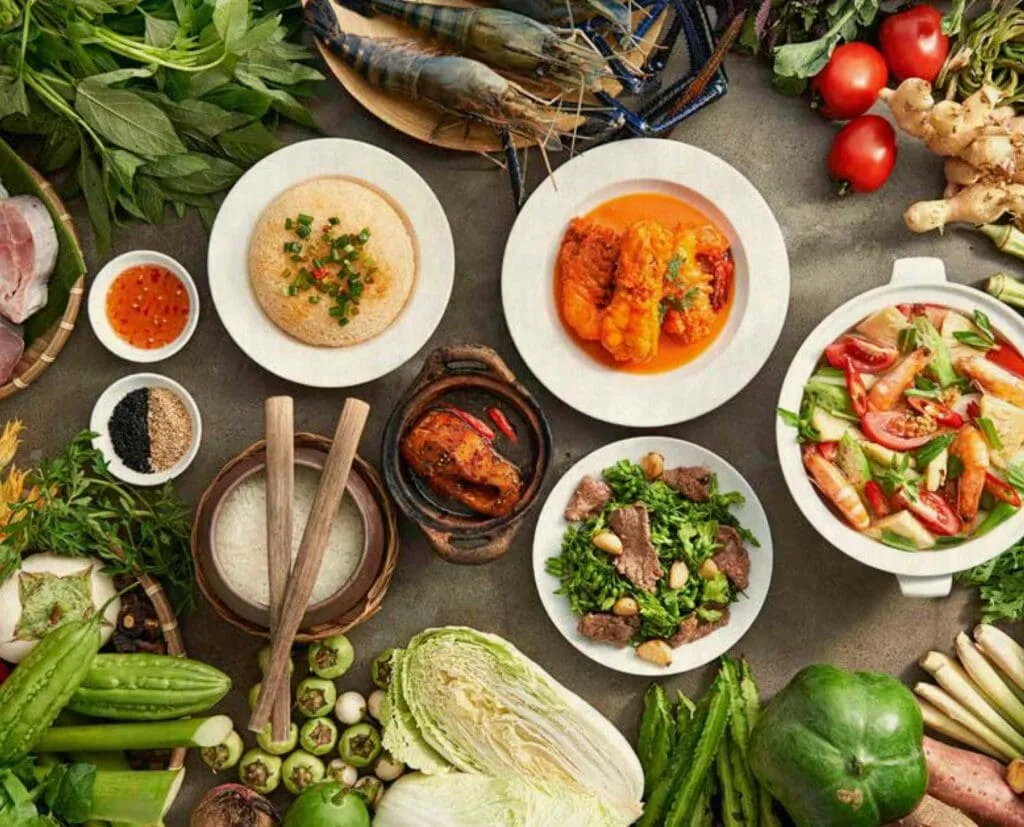 A colorful assortment of traditional Vietnamese dishes at Com Nieu Saigon, including clay pot fish, sour soup, crispy rice, and fresh vegetables