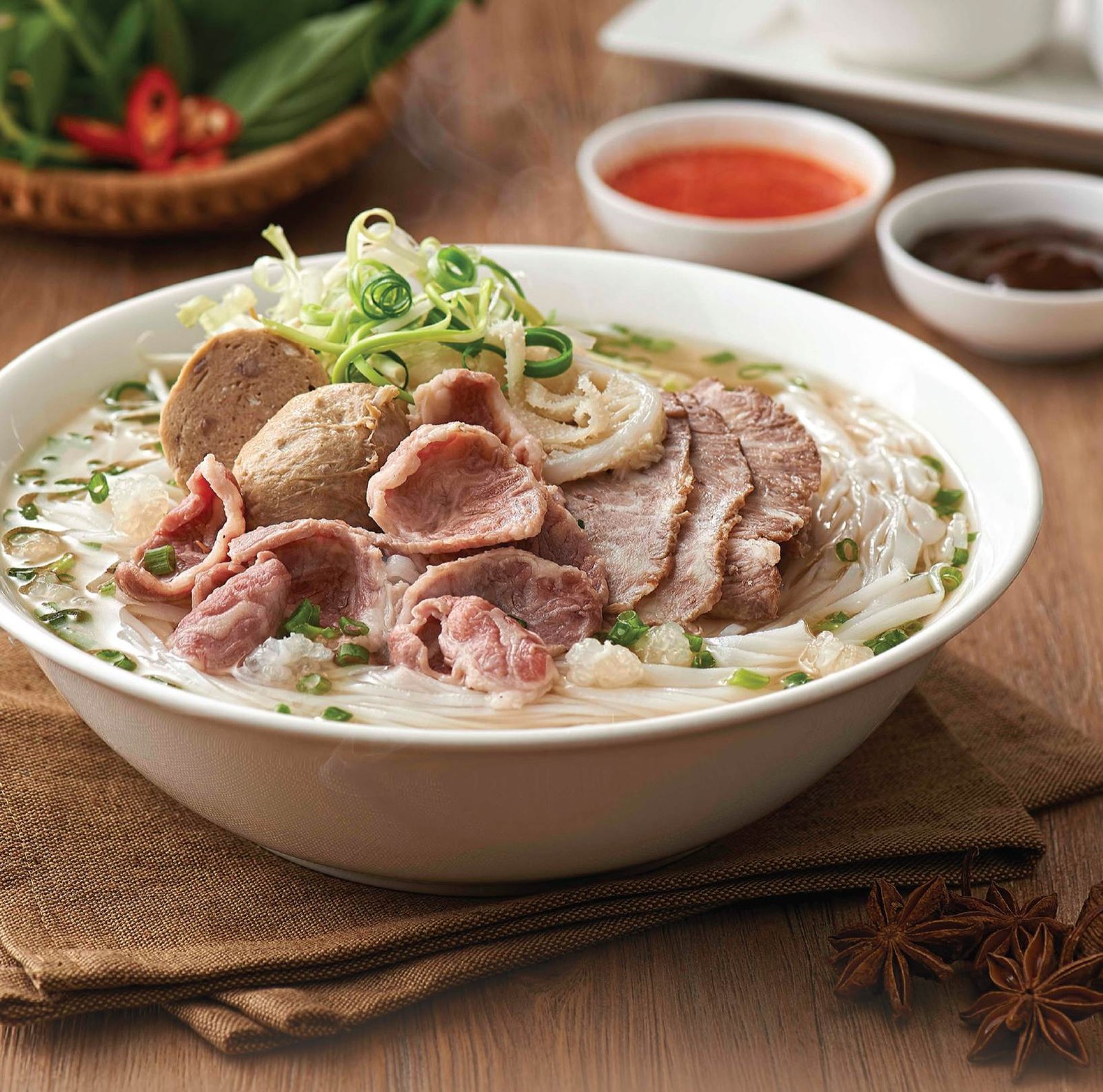 A steaming bowl of Pho Bo (Vietnamese beef noodle soup) served for breakfast at Com Nieu Saigon with rare beef slices, meatballs, and fresh herbs