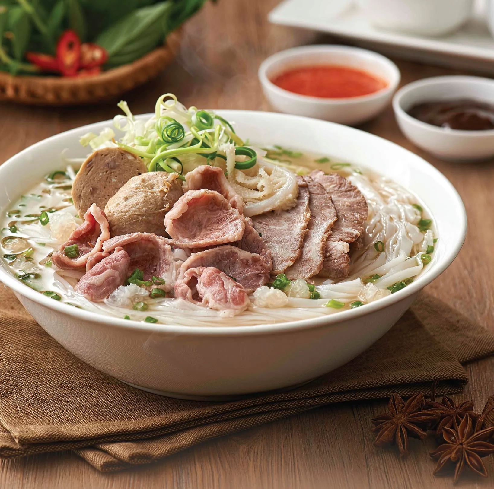 A steaming bowl of Pho Bo (Vietnamese beef noodle soup) served for breakfast at Com Nieu Saigon with rare beef slices, meatballs, and fresh herbs