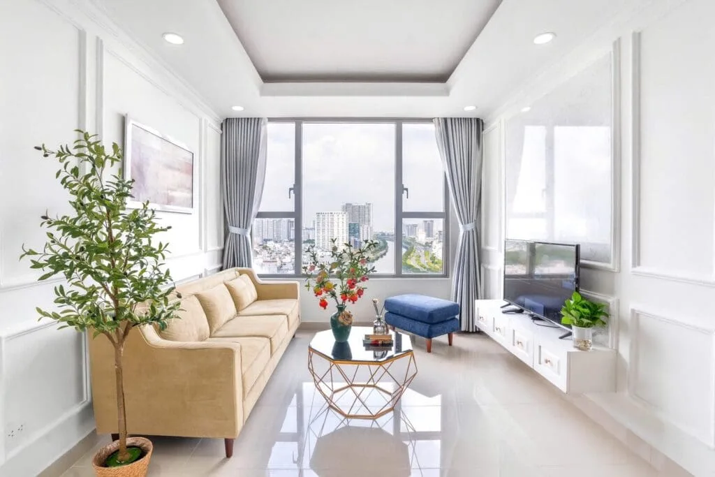 Phòng khách căn hộ 2 phòng ngủ tại RiverGate Residence, thiết kế sang trọng, đầy đủ tiện nghi với sofa, TV, cửa sổ lớn view sông Bến Nghé – lựa chọn lý tưởng cho gia đình Việt kiều 3–4 người.